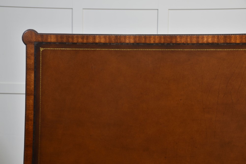 An antique mahogany writing table featuring three frieze drawers with brass handles, a leather inset top, and slim reeded legs with brass castors. View XV