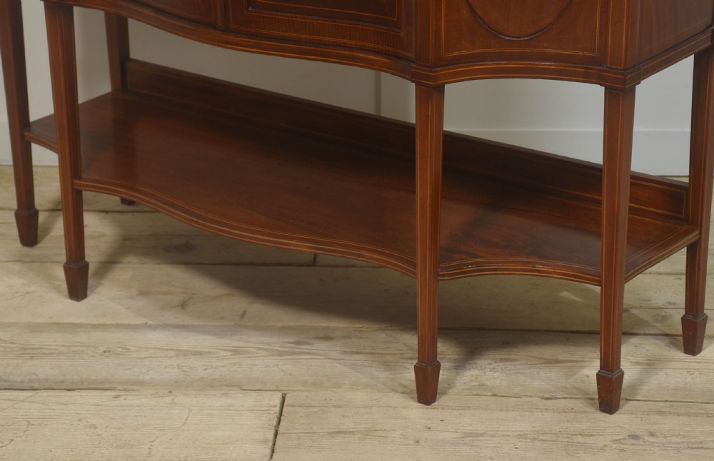 An Edwardian inlaid mahogany display cabinet featuring a swan-neck pediment, glass shelves, inlaid floral marquetry doors, and slender tapered legs. View VII