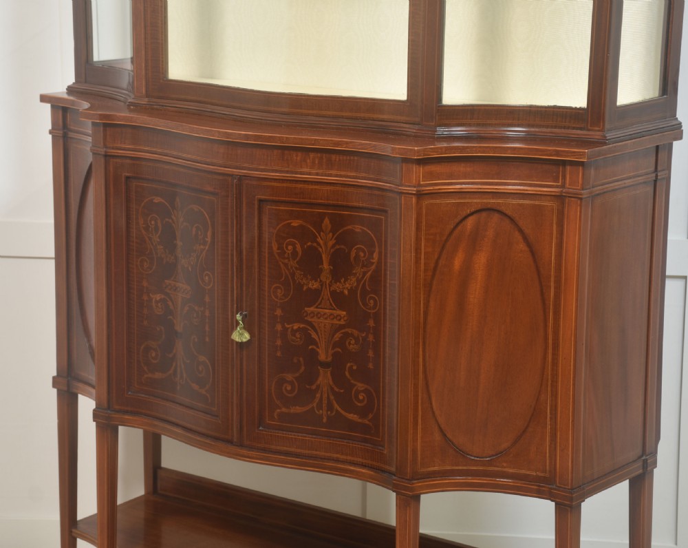 An Edwardian inlaid mahogany display cabinet featuring a swan-neck pediment, glass shelves, inlaid floral marquetry doors, and slender tapered legs. View VIII