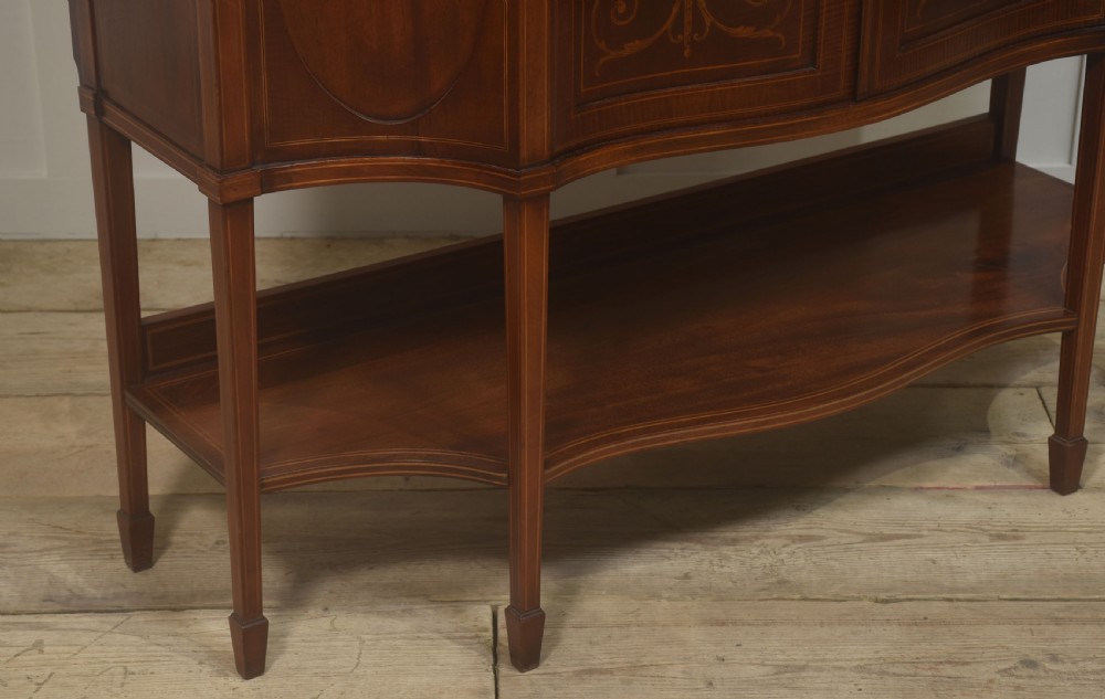 An Edwardian inlaid mahogany display cabinet featuring a swan-neck pediment, glass shelves, inlaid floral marquetry doors, and slender tapered legs. View XI