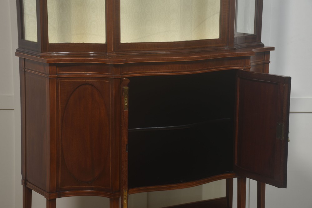 An Edwardian inlaid mahogany display cabinet featuring a swan-neck pediment, glass shelves, inlaid floral marquetry doors, and slender tapered legs. View XII