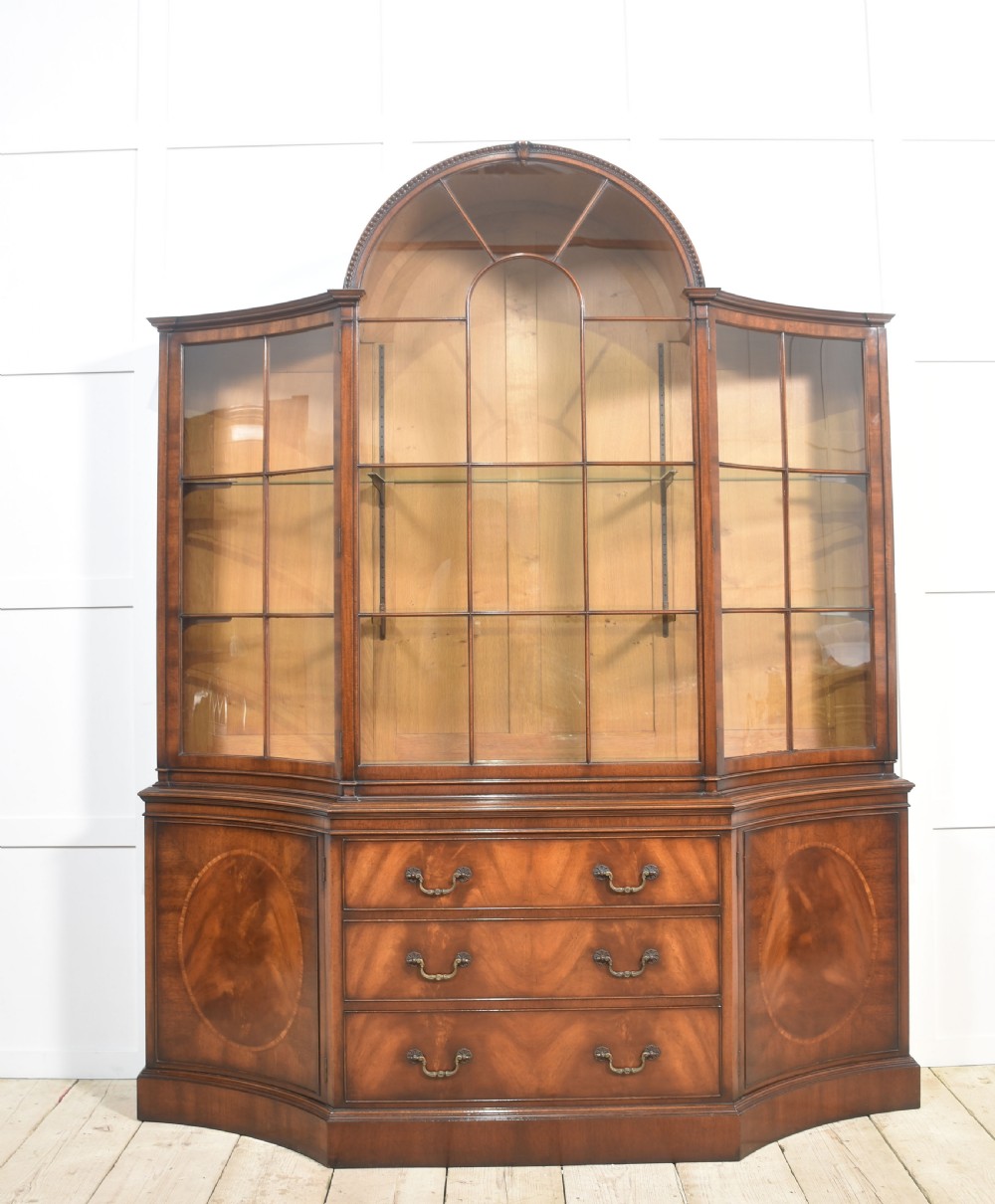 A large mahogany glazed display cabinet featuring an arched central section with glass doors, flame mahogany drawer fronts, and oval inlaid cupboard panels.