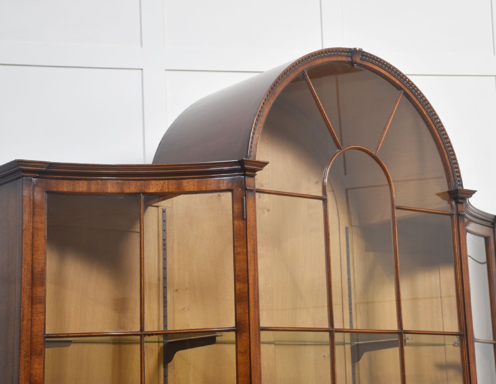 A large mahogany glazed display cabinet featuring an arched central section with glass doors, flame mahogany drawer fronts, and oval inlaid cupboard panels. View IX