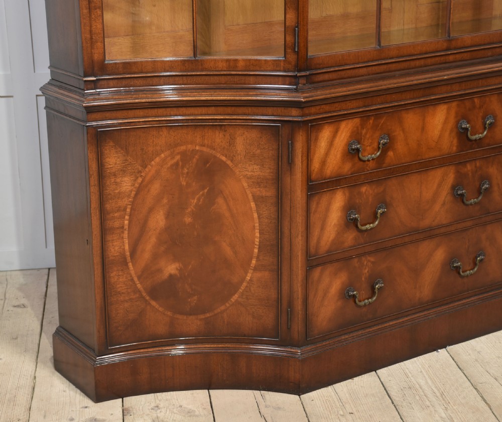 A large mahogany glazed display cabinet featuring an arched central section with glass doors, flame mahogany drawer fronts, and oval inlaid cupboard panels. View X