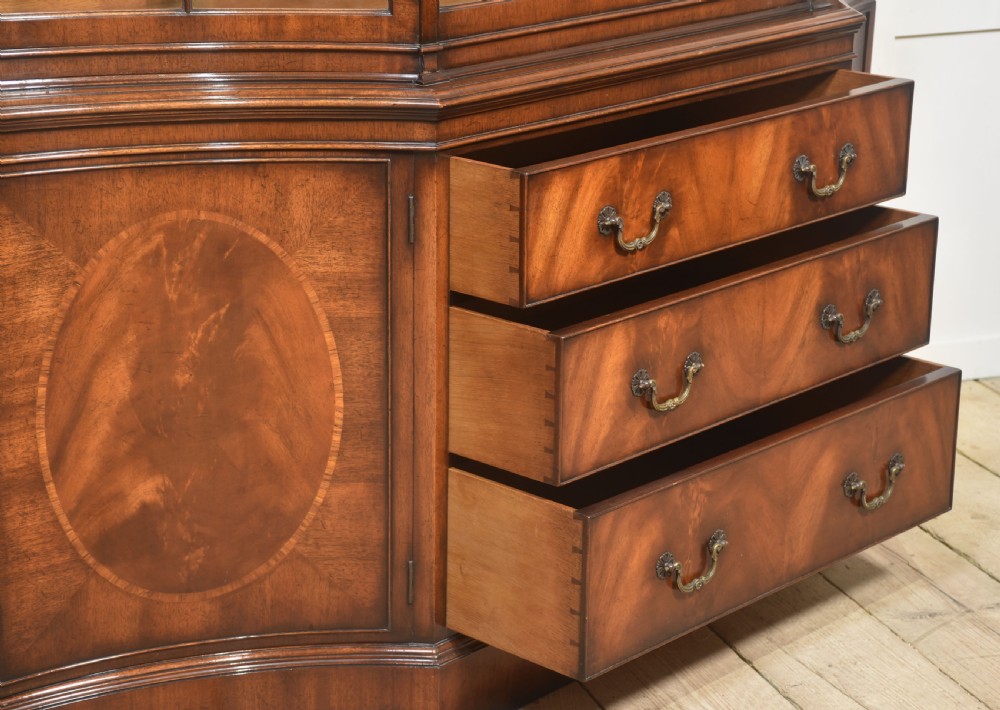 A large mahogany glazed display cabinet featuring an arched central section with glass doors, flame mahogany drawer fronts, and oval inlaid cupboard panels. View XII