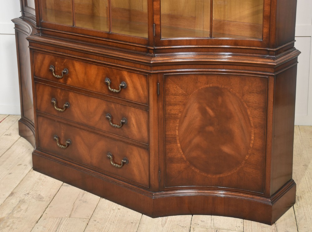 A large mahogany glazed display cabinet featuring an arched central section with glass doors, flame mahogany drawer fronts, and oval inlaid cupboard panels. View XV