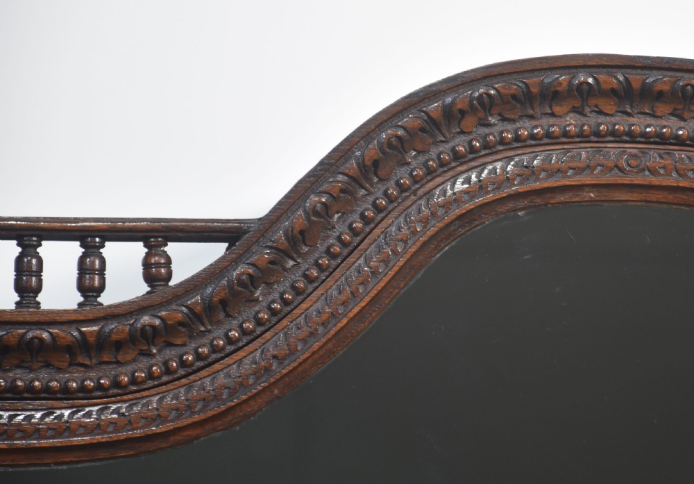 A dark carved oak display cabinet featuring a large upper glazed section with an arched spindle gallery top above two deeply relief-carved cupboard doors. View VII