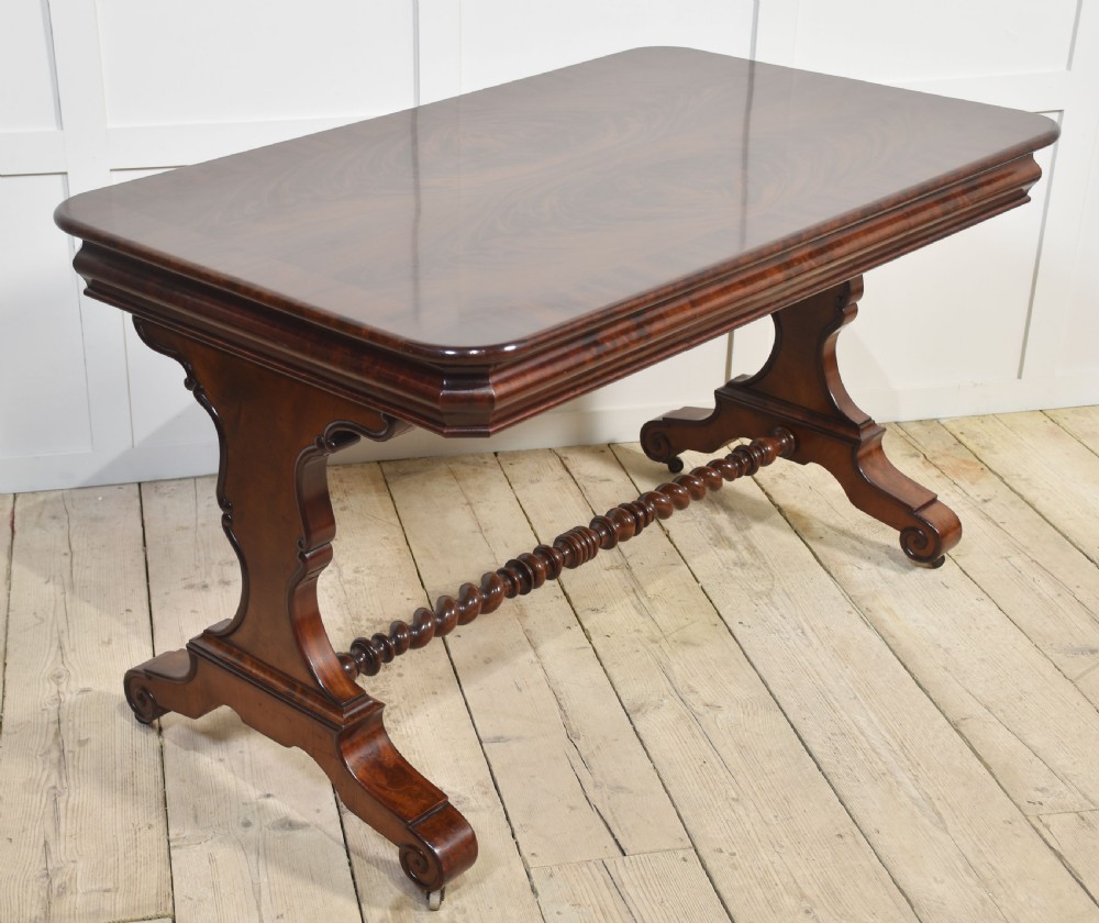 A Victorian mahogany centre table featuring a polished rectangular top with rounded corners, trestle end supports, a spiral-turned stretcher, and scroll feet on castors.