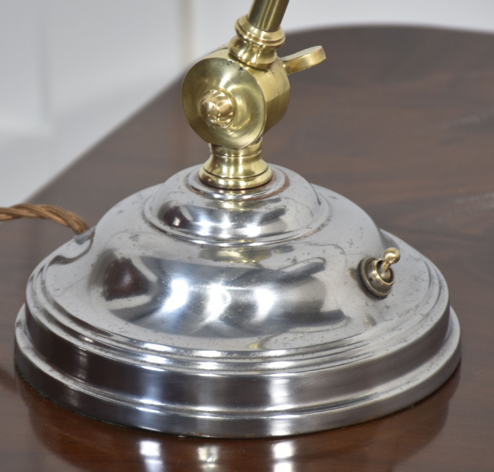 An adjustable metal bankers desk lamp featuring a curved silver-tone shade, brass support arm with a wingnut joint, and a polished circular base. View III