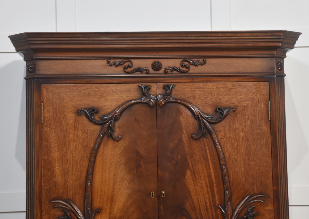 A tall carved mahogany linen press featuring upper double doors with carved leaf motifs over a chest with three drawers. View III