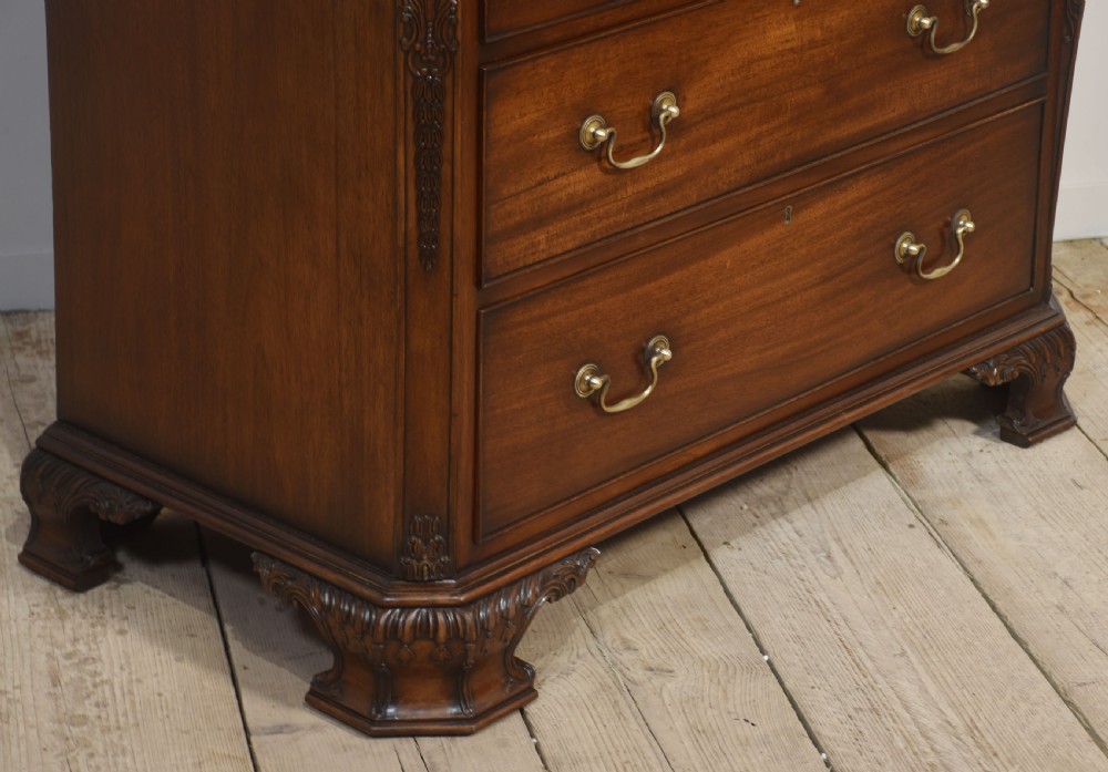 A tall carved mahogany linen press featuring upper double doors with carved leaf motifs over a chest with three drawers. View VIII