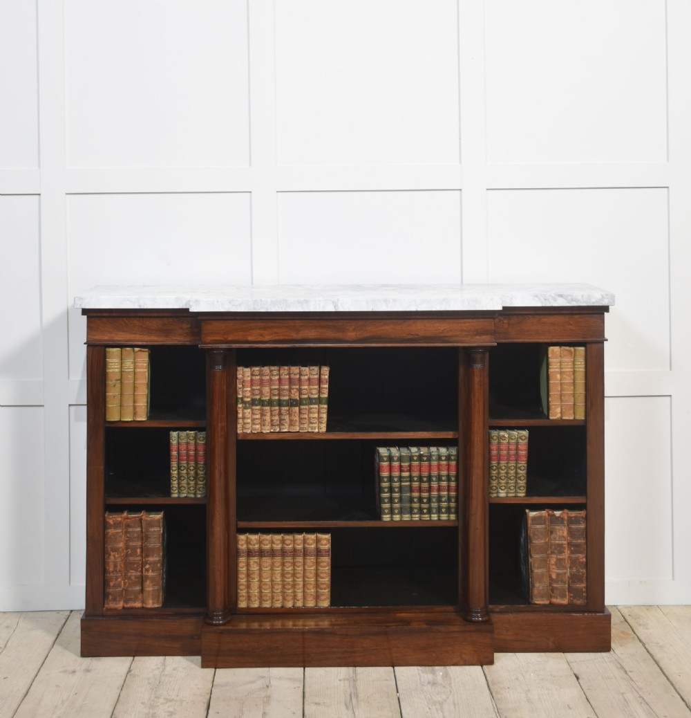 A 19th-century rosewood breakfront open bookcase featuring a pale marble top surface and decorative turned columns flanking open shelves filled with books.