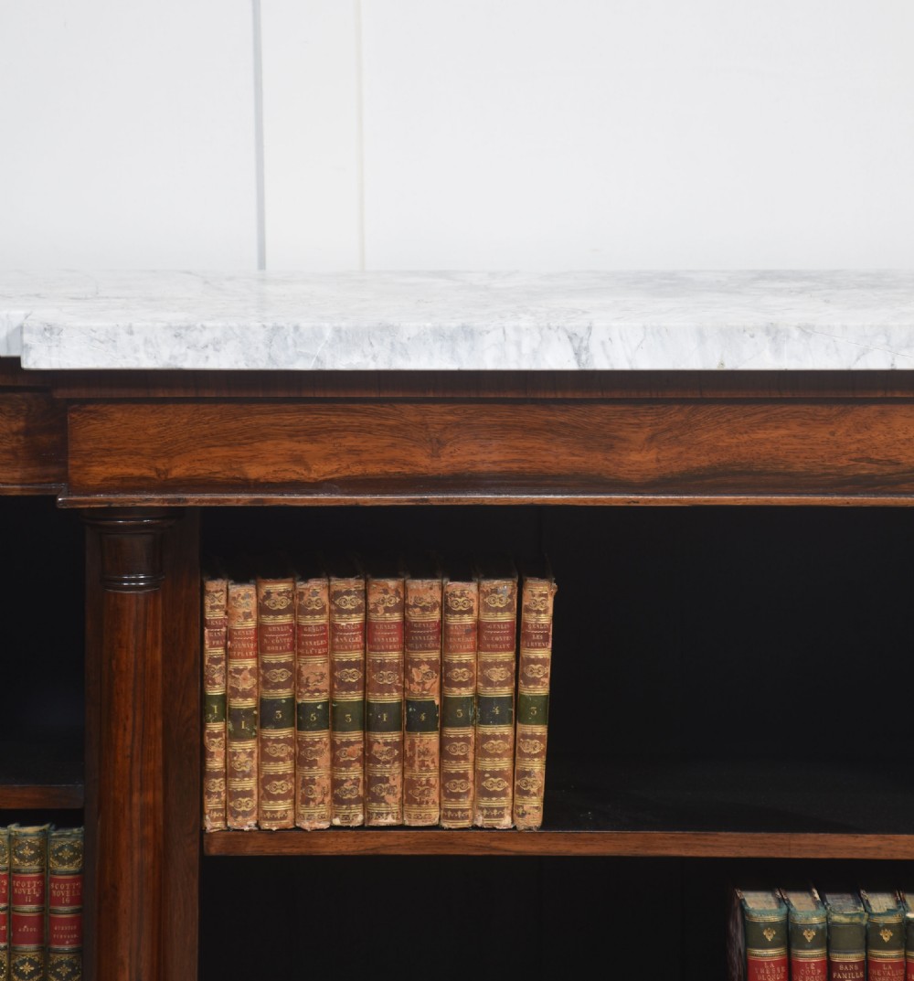 A 19th-century rosewood breakfront open bookcase featuring a pale marble top surface and decorative turned columns flanking open shelves filled with books. View II