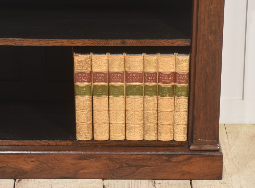 A 19th-century rosewood open bookcase featuring three open shelves, carved corner rosettes, pilasters, and a solid plinth base. View VI
