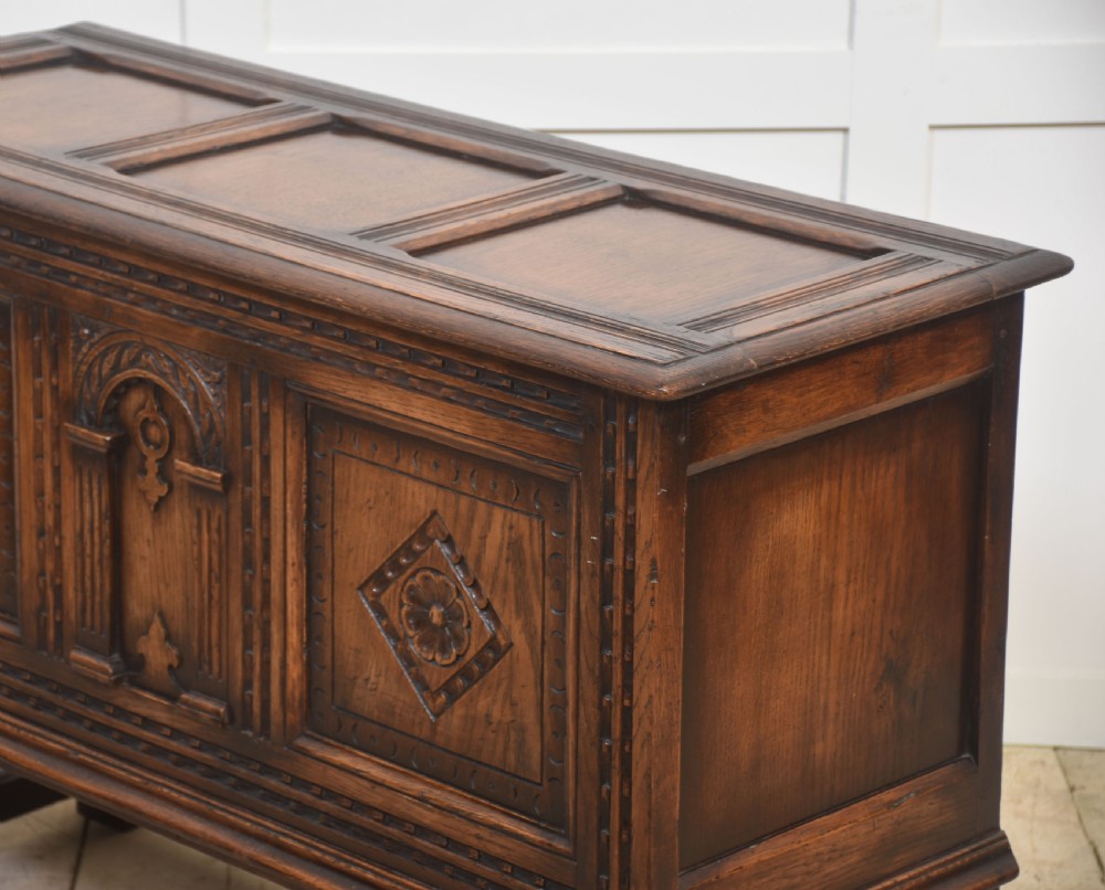 A dark carved oak coffer featuring three decorative front panels, turned legs, and a lower stretcher base. View XII