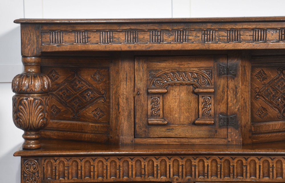 A two-tiered carved oak court cupboard featuring recessed upper doors flanked by bulbous turned supports and lower panelled doors adorned with carved arches. View II