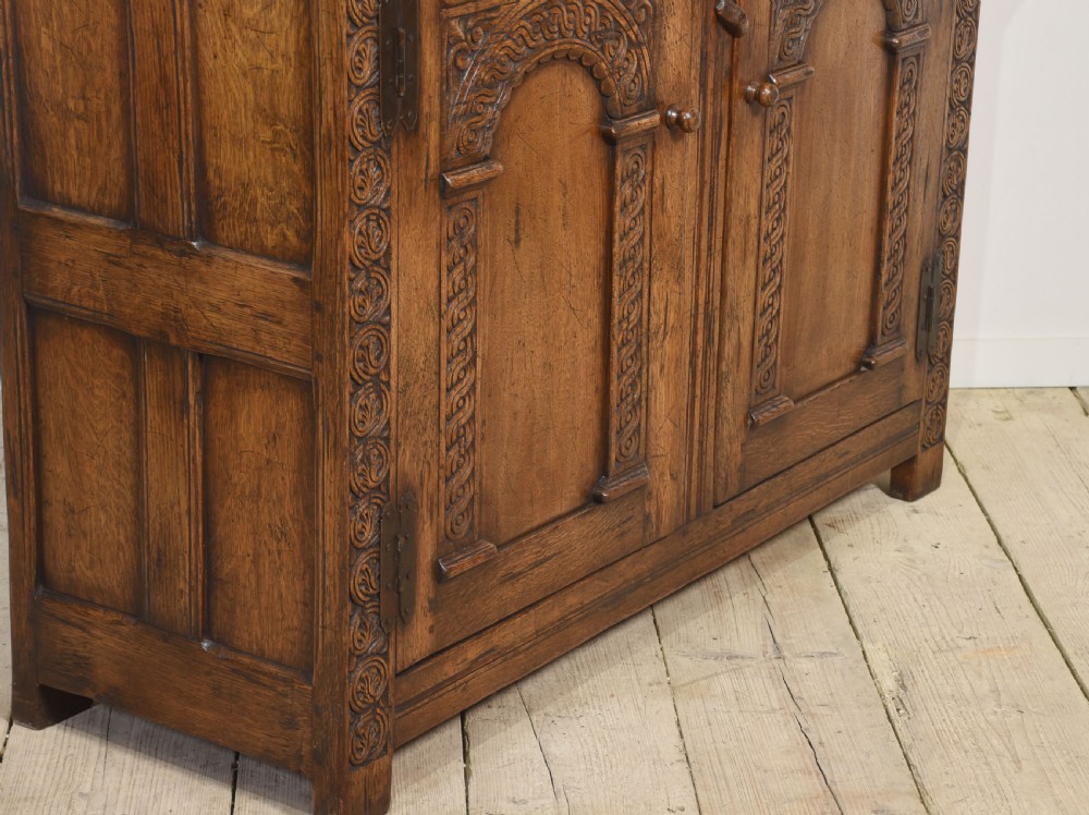 A two-tiered carved oak court cupboard featuring recessed upper doors flanked by bulbous turned supports and lower panelled doors adorned with carved arches. View XI