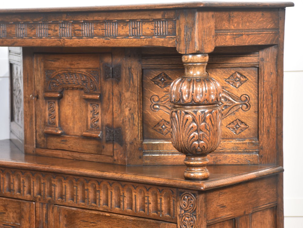 A two-tiered carved oak court cupboard featuring recessed upper doors flanked by bulbous turned supports and lower panelled doors adorned with carved arches. View XIV