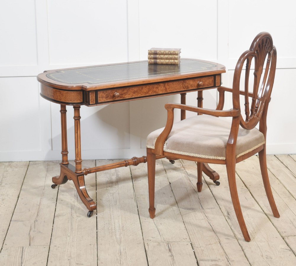 A Victorian burr walnut writing table featuring a green leather inset top with gold tooling, a single drawer, turned legs, a central stretcher, and brass castors. View II