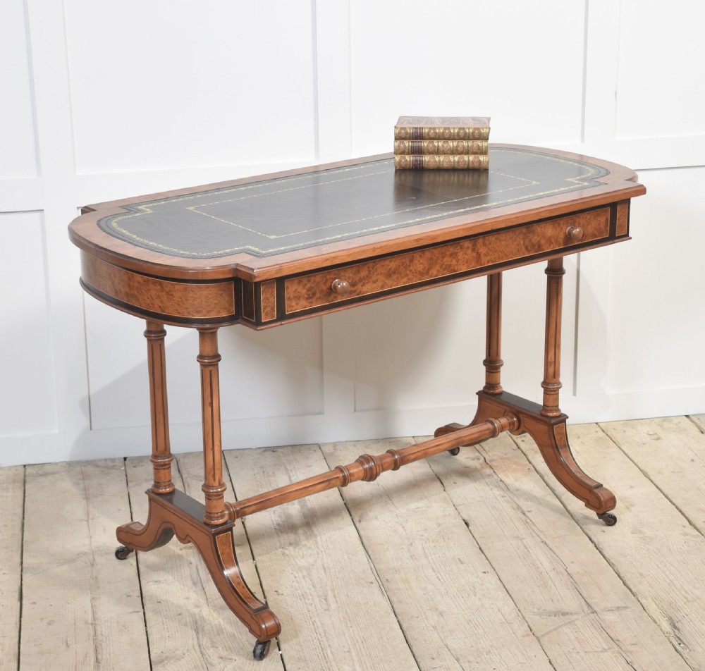 A Victorian burr walnut writing table featuring a green leather inset top with gold tooling, a single drawer, turned legs, a central stretcher, and brass castors. View III