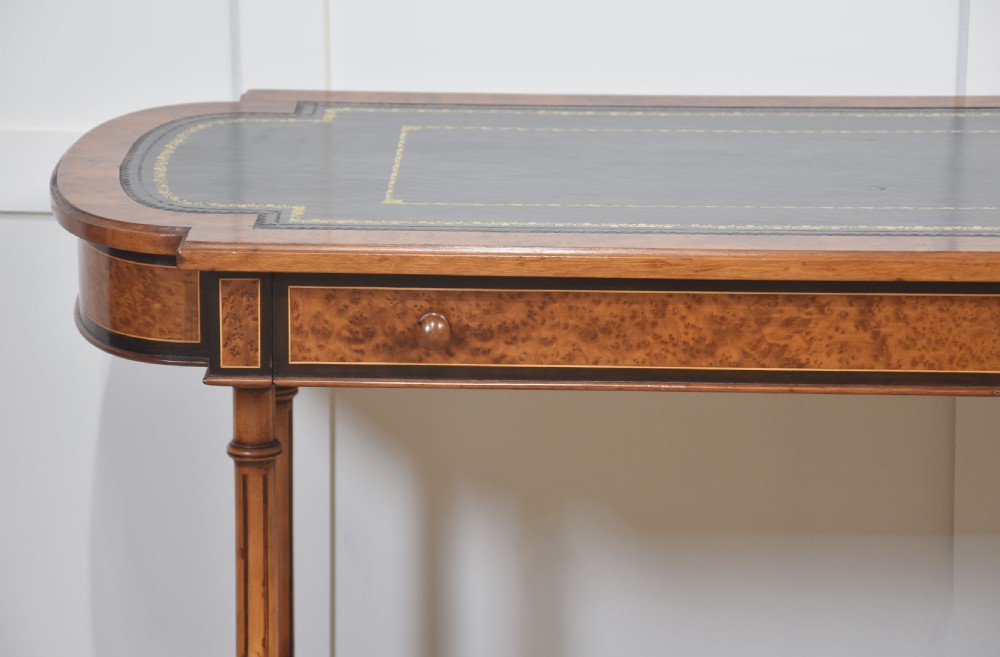 A Victorian burr walnut writing table featuring a green leather inset top with gold tooling, a single drawer, turned legs, a central stretcher, and brass castors. View VII