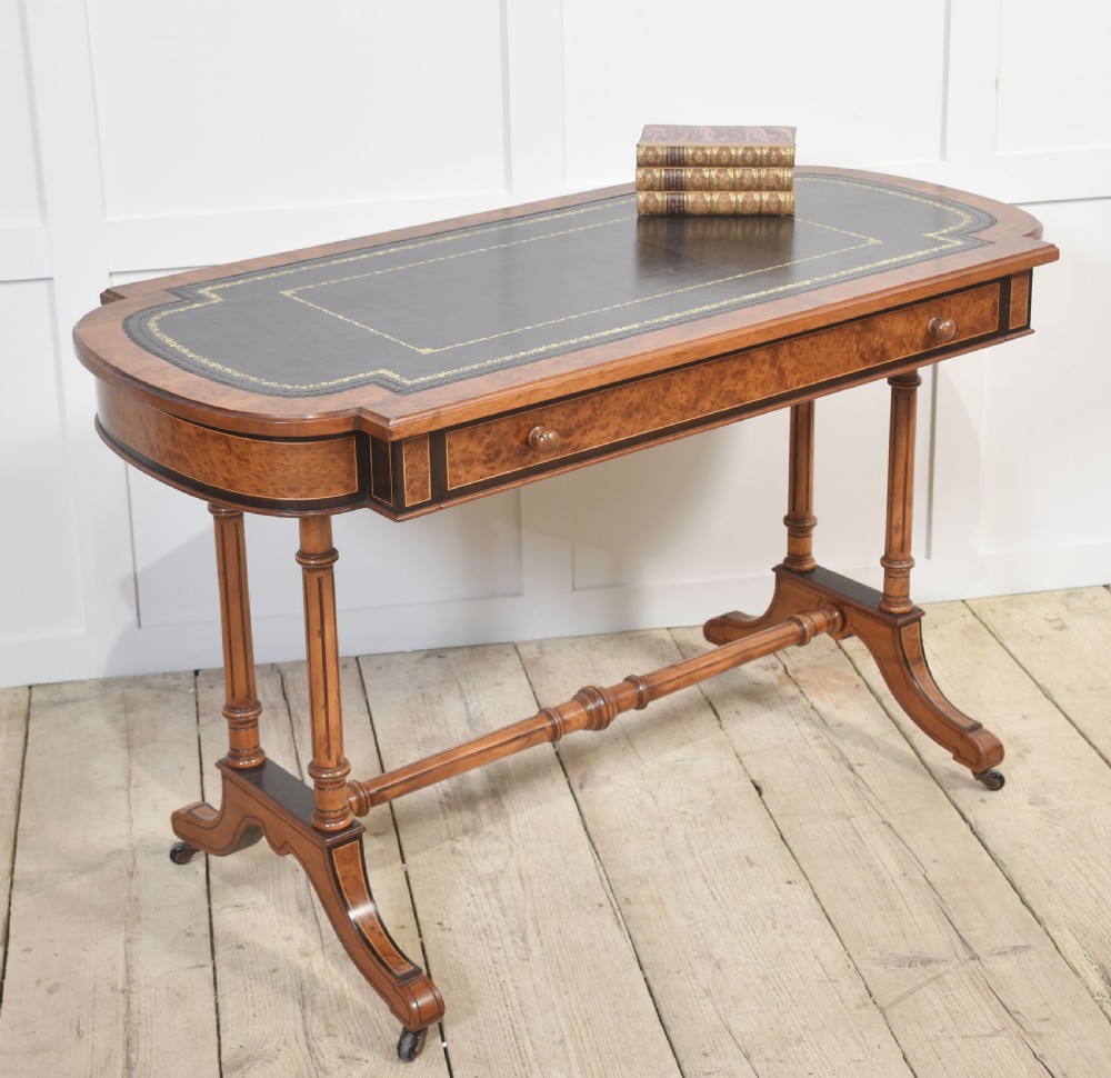 A Victorian burr walnut writing table featuring a green leather inset top with gold tooling, a single drawer, turned legs, a central stretcher, and brass castors. View VIII