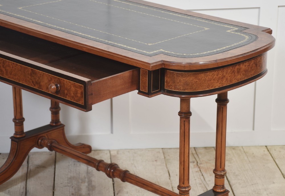 A Victorian burr walnut writing table featuring a green leather inset top with gold tooling, a single drawer, turned legs, a central stretcher, and brass castors. View XI