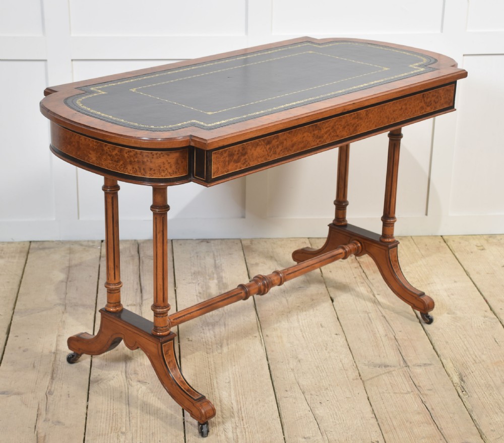 A Victorian burr walnut writing table featuring a green leather inset top with gold tooling, a single drawer, turned legs, a central stretcher, and brass castors. View XII