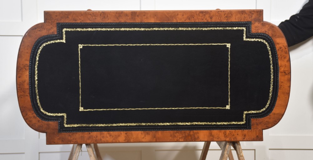 A Victorian burr walnut writing table featuring a green leather inset top with gold tooling, a single drawer, turned legs, a central stretcher, and brass castors. View XIII