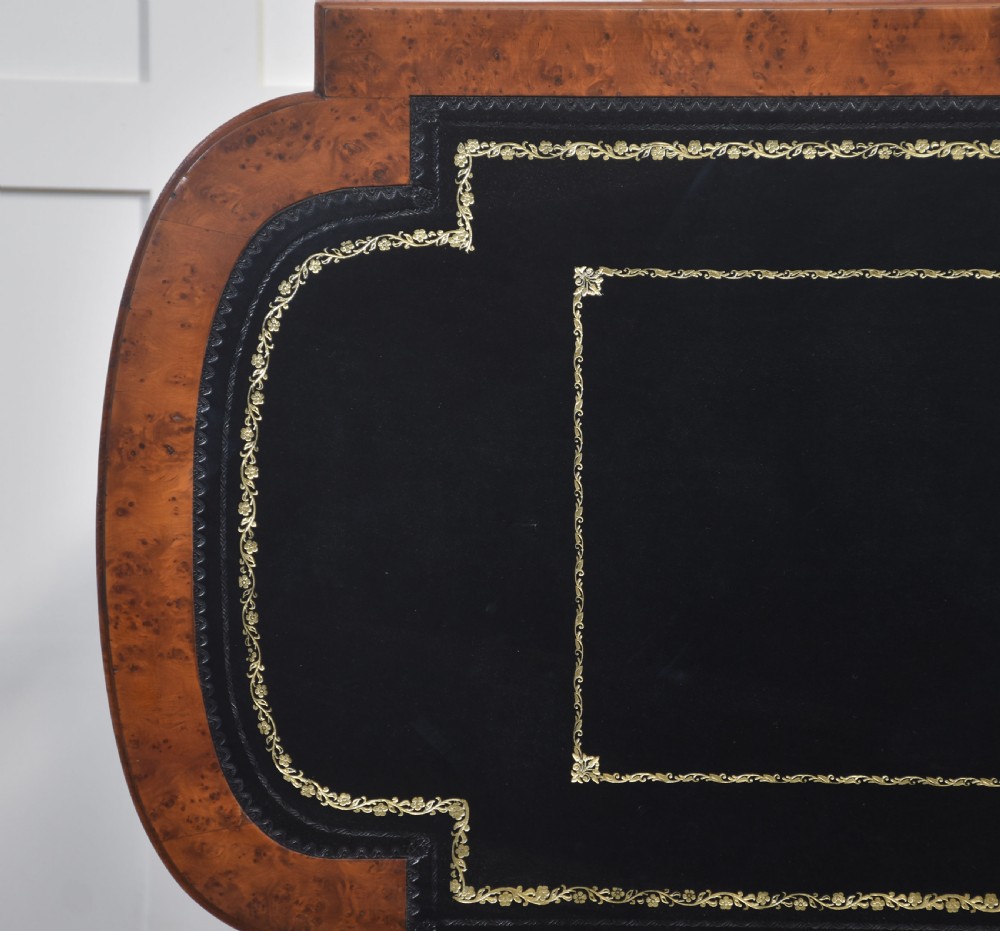 A Victorian burr walnut writing table featuring a green leather inset top with gold tooling, a single drawer, turned legs, a central stretcher, and brass castors. View XIV