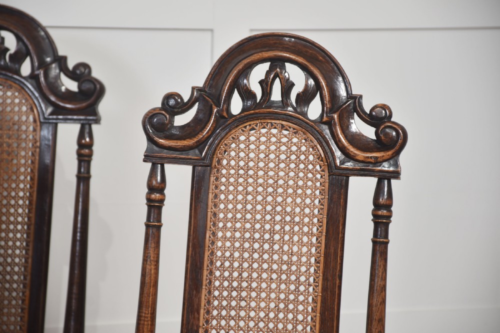 Set of eight carved dark oak high-back dining chairs with woven cane backrests and seats, comprising two armchairs and six side chairs. View IV