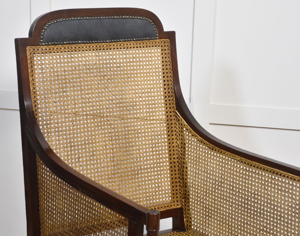 A Regency mahogany bergere armchair with hand-woven cane side panels, turned front legs on brass castors, and dark grey fabric cushions. View XII