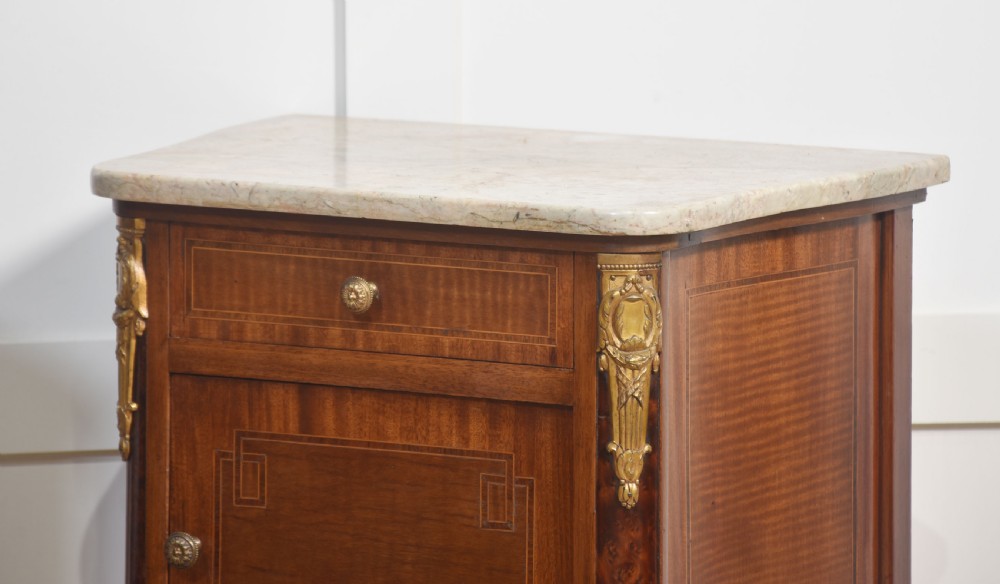 A pair of French Louis XVI style mahogany bedside cabinets featuring pale marble tops, gilt metal corner mounts, single drawers, and slender turned legs. View III