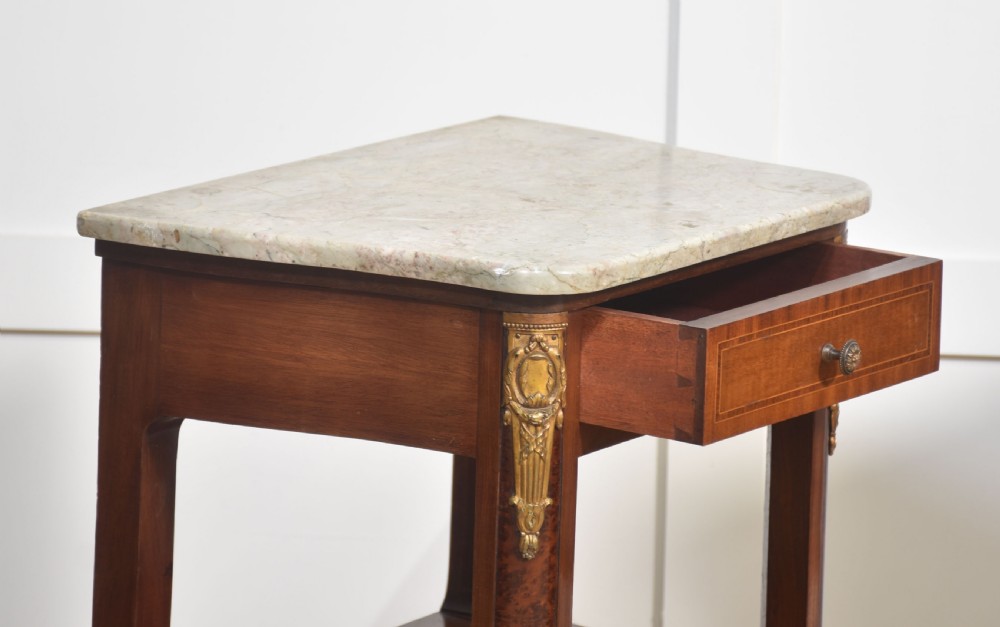 A pair of French Louis XVI style mahogany bedside cabinets featuring pale marble tops, gilt metal corner mounts, single drawers, and slender turned legs. View XII