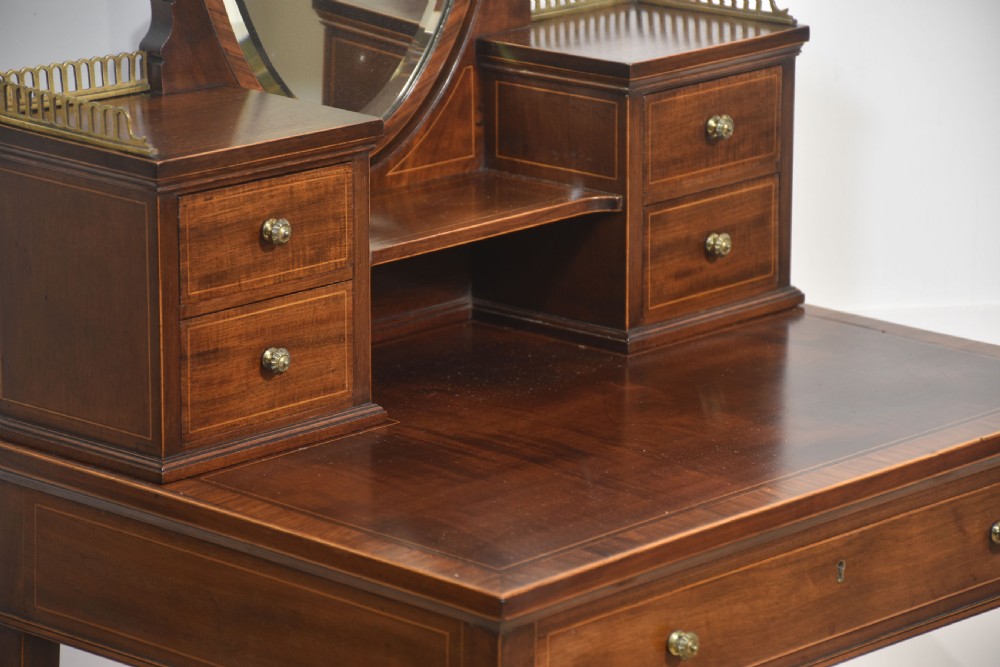 An antique mahogany dressing table with an integrated shield-shaped mirror, twin trinket drawers with brass galleries, a central drawer, and tall tapered legs. View V