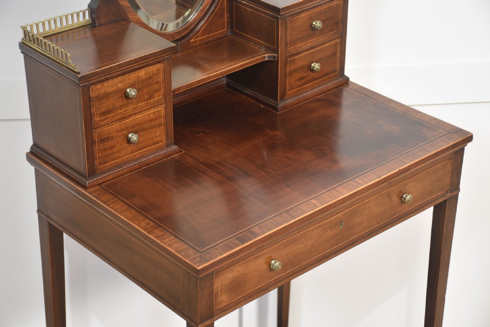 An antique mahogany dressing table with an integrated shield-shaped mirror, twin trinket drawers with brass galleries, a central drawer, and tall tapered legs. View VI