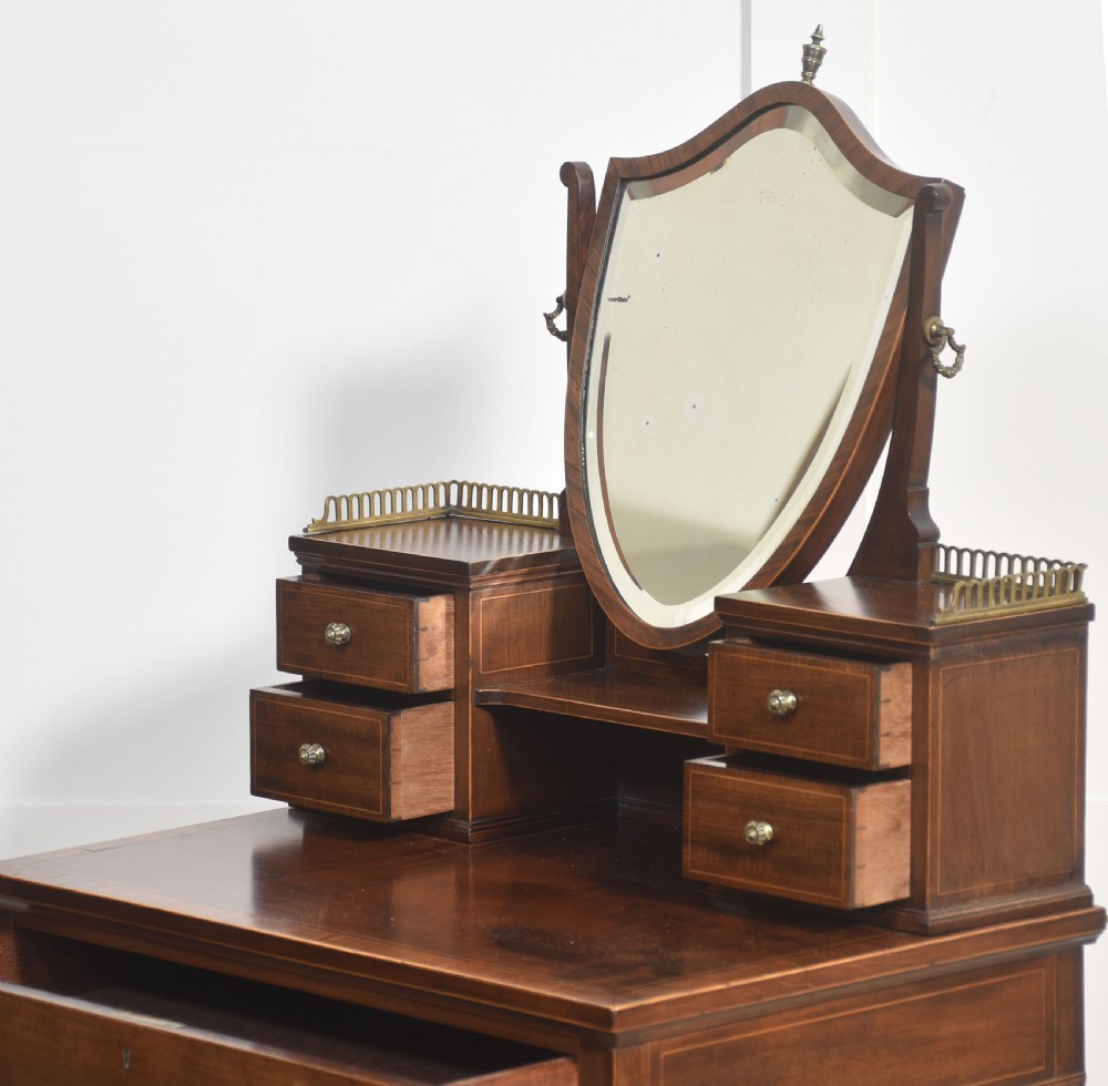 An antique mahogany dressing table with an integrated shield-shaped mirror, twin trinket drawers with brass galleries, a central drawer, and tall tapered legs. View XII