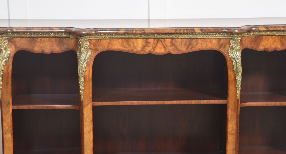 An antique figured walnut breakfront open bookcase featuring three shelf compartments and ornamental gilt metal mounts along the frieze and pilasters. View V