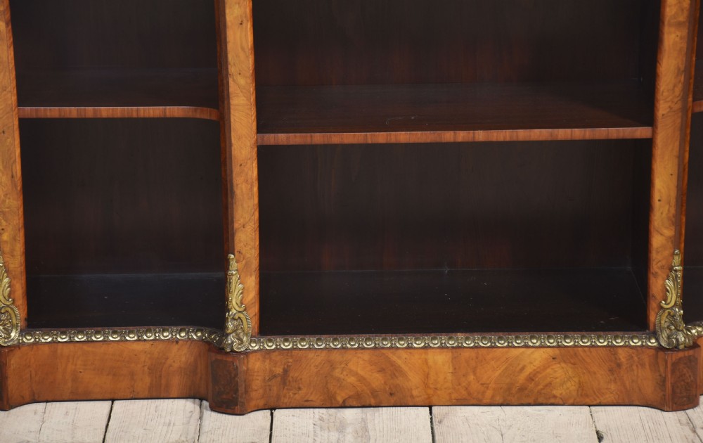 An antique figured walnut breakfront open bookcase featuring three shelf compartments and ornamental gilt metal mounts along the frieze and pilasters. View VI