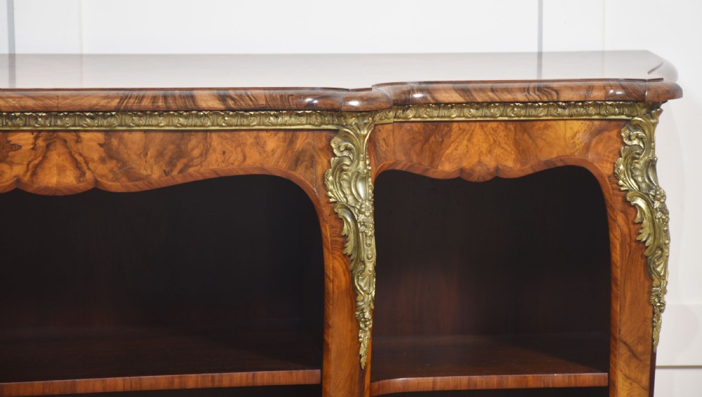 An antique figured walnut breakfront open bookcase featuring three shelf compartments and ornamental gilt metal mounts along the frieze and pilasters. View VII