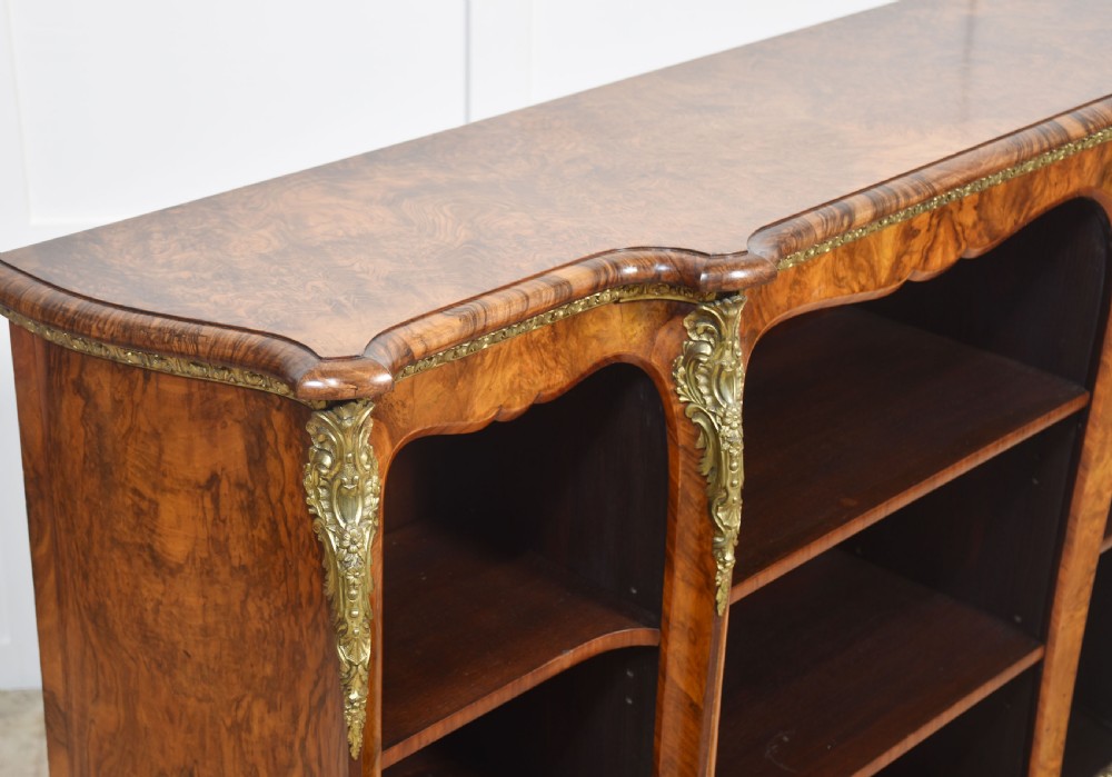 An antique figured walnut breakfront open bookcase featuring three shelf compartments and ornamental gilt metal mounts along the frieze and pilasters. View IX