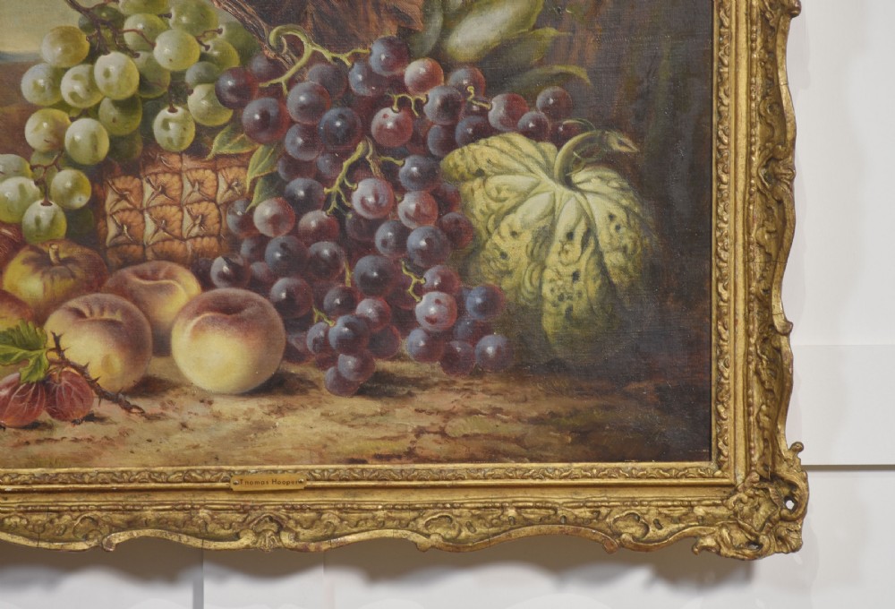 An antique oil on canvas still life painting depicting an arrangement of grapes, peaches, and melons within an ornate gilded frame. View VI