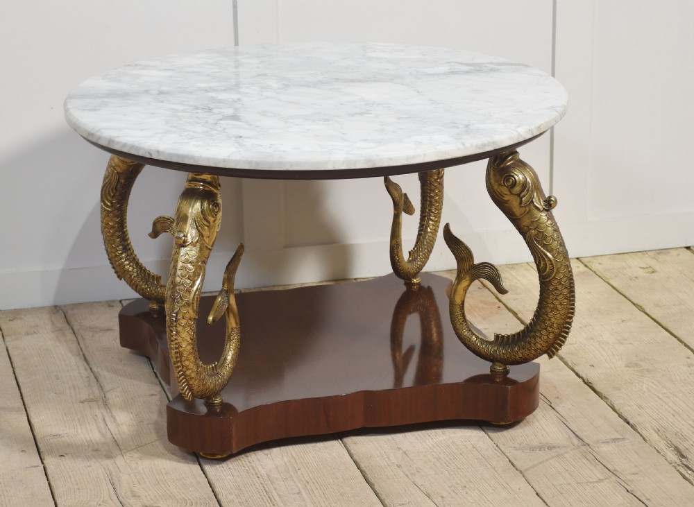 A circular white marble coffee table supported by four cast gilt metal dolphin legs on a dark wooden base.