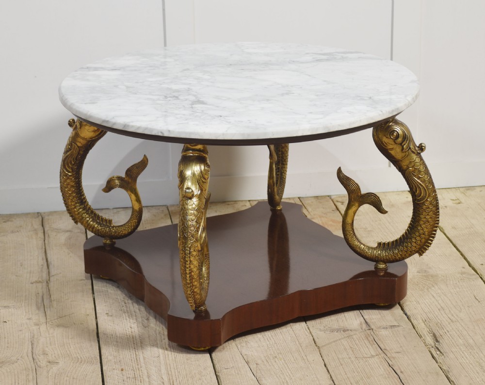 A circular white marble coffee table supported by four cast gilt metal dolphin legs on a dark wooden base. View VI