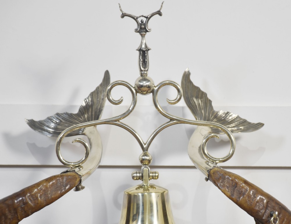 A 19th-century desk inkstand constructed from two curved natural horns, fitted with silvered dolphin-head mounts, inkwells, and a central suspended brass bell on a polished wooden base. View II