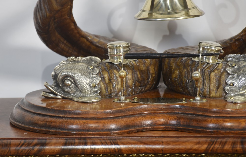 A 19th-century desk inkstand constructed from two curved natural horns, fitted with silvered dolphin-head mounts, inkwells, and a central suspended brass bell on a polished wooden base. View III