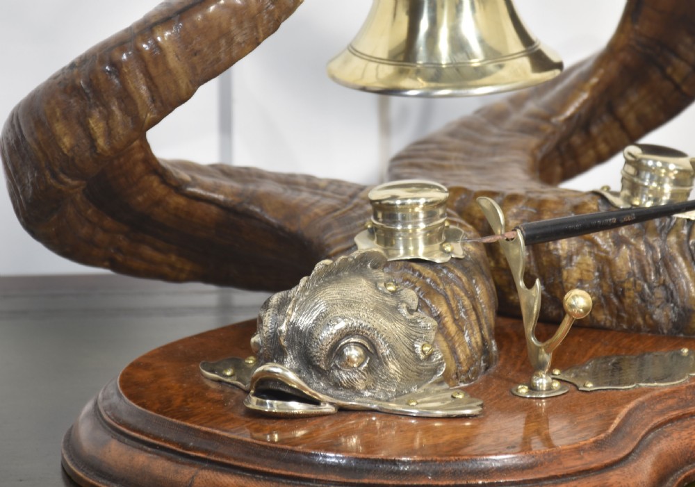 A 19th-century desk inkstand constructed from two curved natural horns, fitted with silvered dolphin-head mounts, inkwells, and a central suspended brass bell on a polished wooden base. View VI
