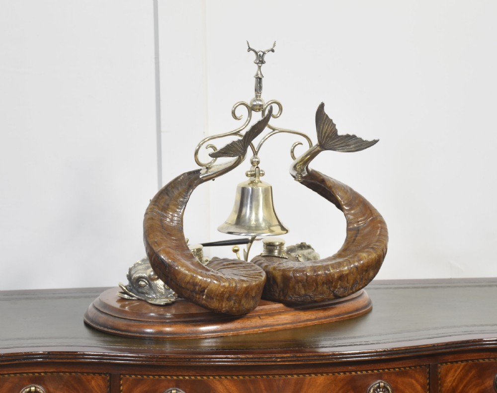 A 19th-century desk inkstand constructed from two curved natural horns, fitted with silvered dolphin-head mounts, inkwells, and a central suspended brass bell on a polished wooden base. View X
