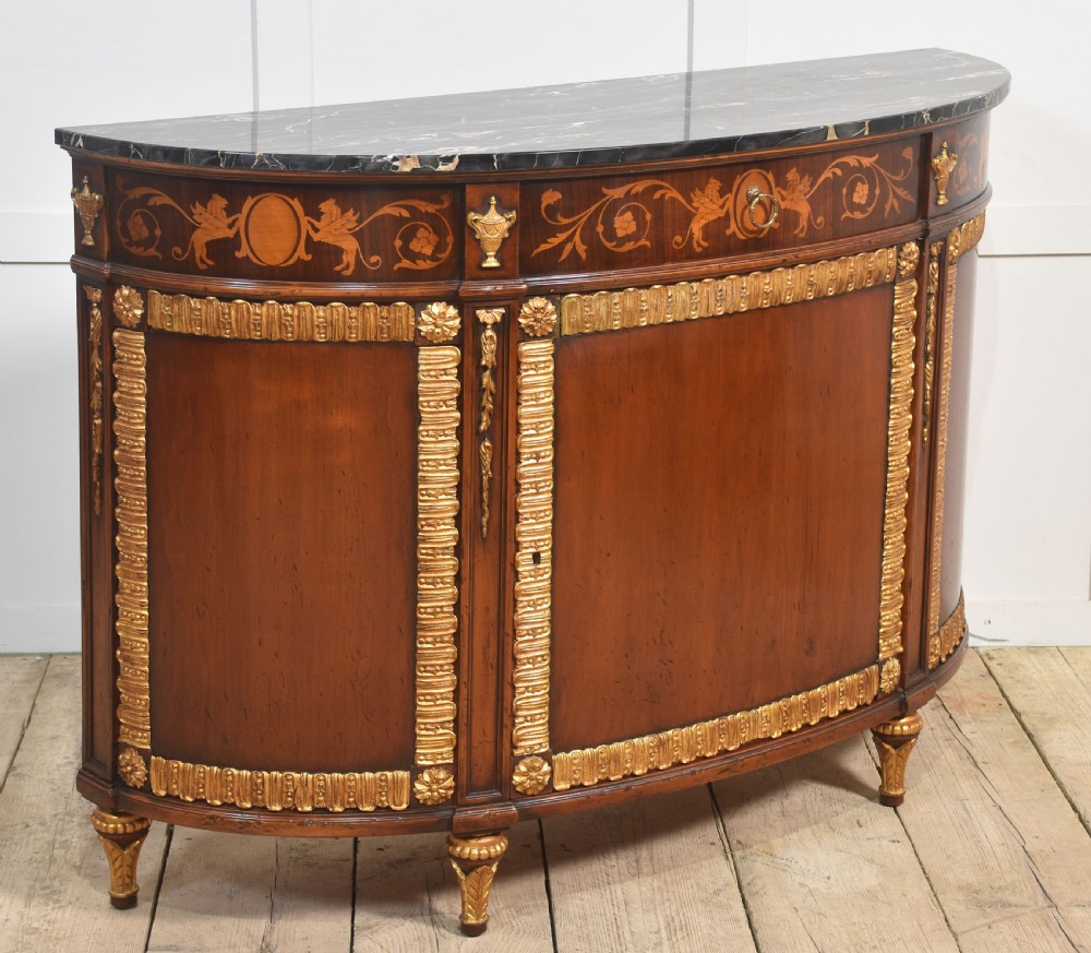 An Italian Neoclassical mahogany bowfront cabinet featuring a black marble top, marquetry frieze with foliate motifs, and carved parcel gilt trims. View V