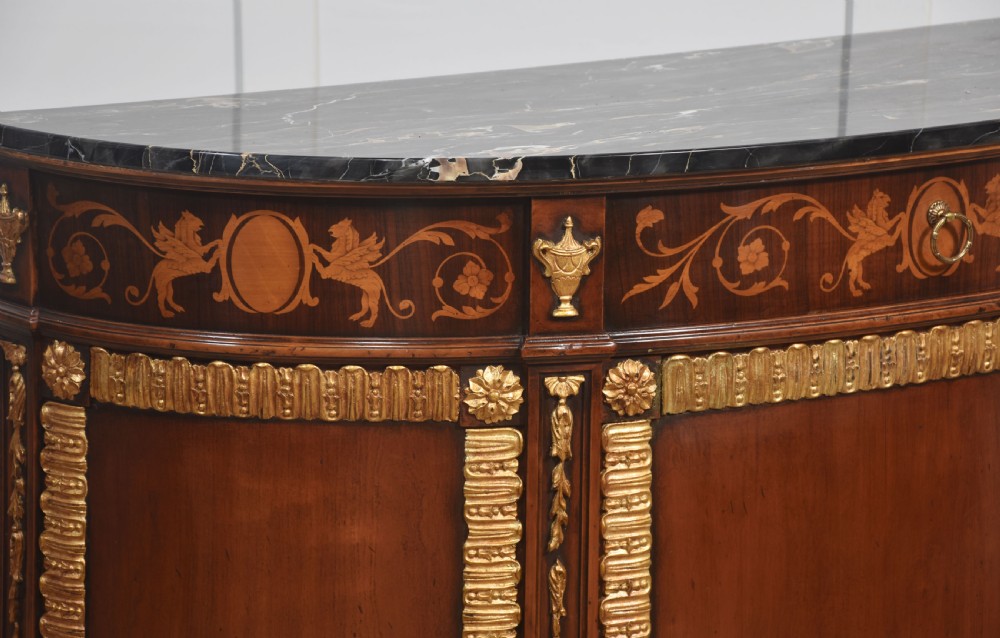 An Italian Neoclassical mahogany bowfront cabinet featuring a black marble top, marquetry frieze with foliate motifs, and carved parcel gilt trims. View VII